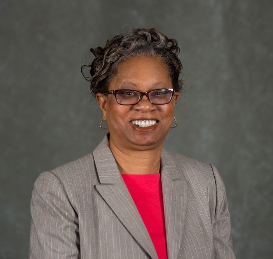 A portrait of Ms. Adams-Cambell in which she is wearing glasses and a gray suit with red shirt