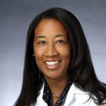 A portrait of Dr. Caskin in a white medical coat, taken against a gray background.