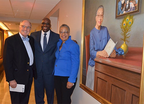 Stephen Ray Mitchell, David Taylor, and Joy Phinizy Williams stand side by side in a hallway next to the portrait of Williams