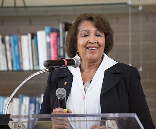 Doris Brown speaks at a podium with shelves of books in the background behind her