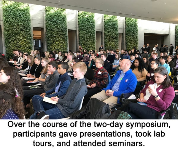 Student participants sit in rows in the audience at the symposium