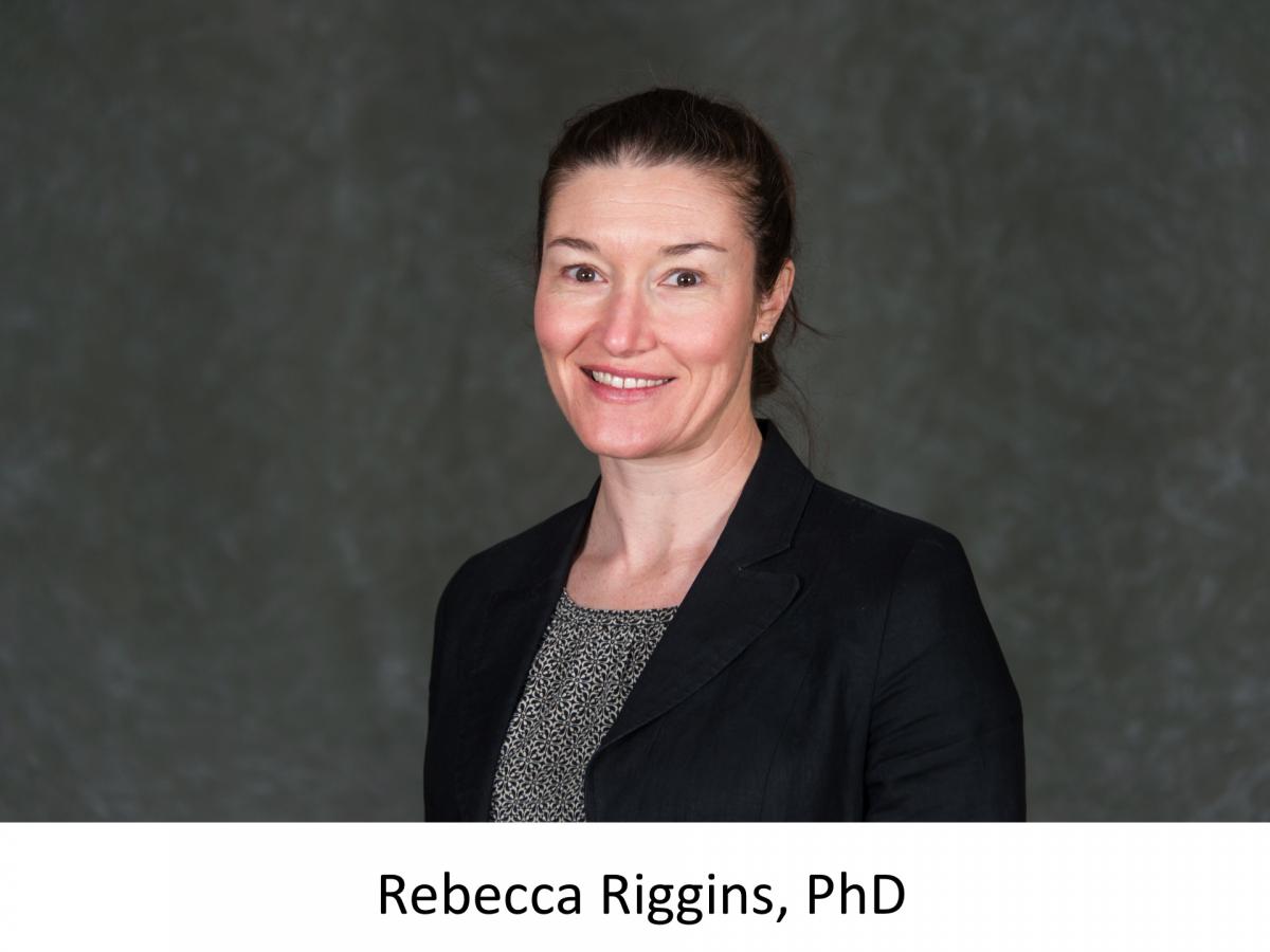 Rebecca Riggins in a grey shirt, black blazer against a grey background