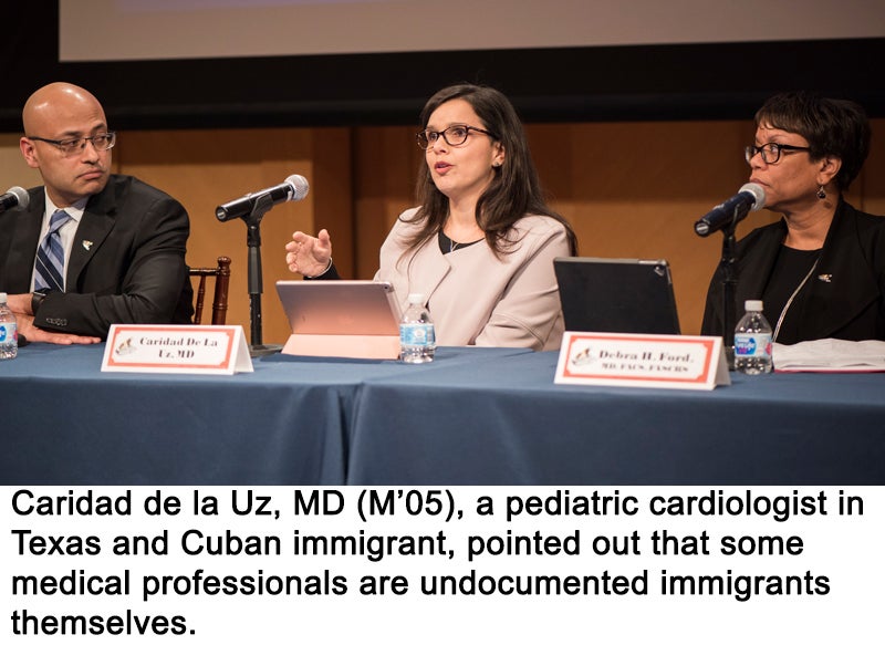 One man and two women sit behind a table. The woman in the center speaks into a microphone.