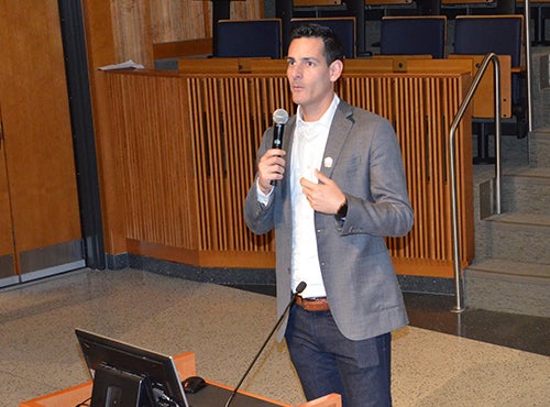 Mike Eisenberg speaks into a microphone while standing in an auditorium next to a podium