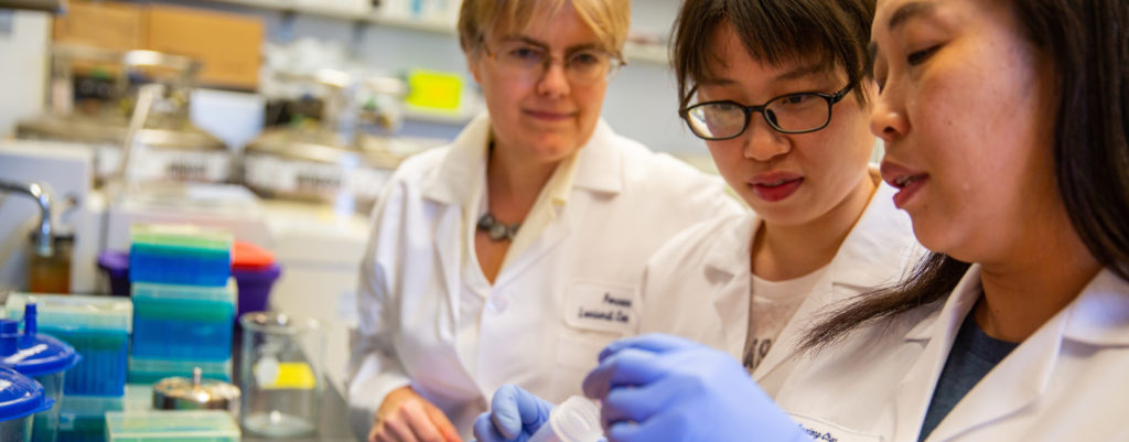 A trio of female researchers consult in a lab