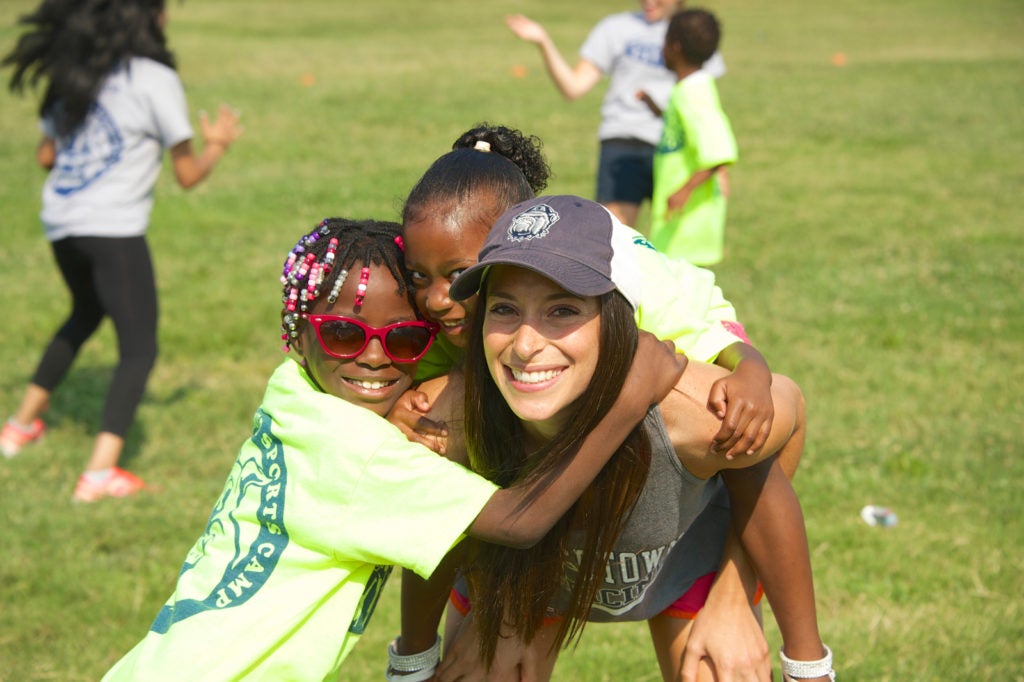 A female medical student gets hugs from two girls participating in the summer camp run by SOM students