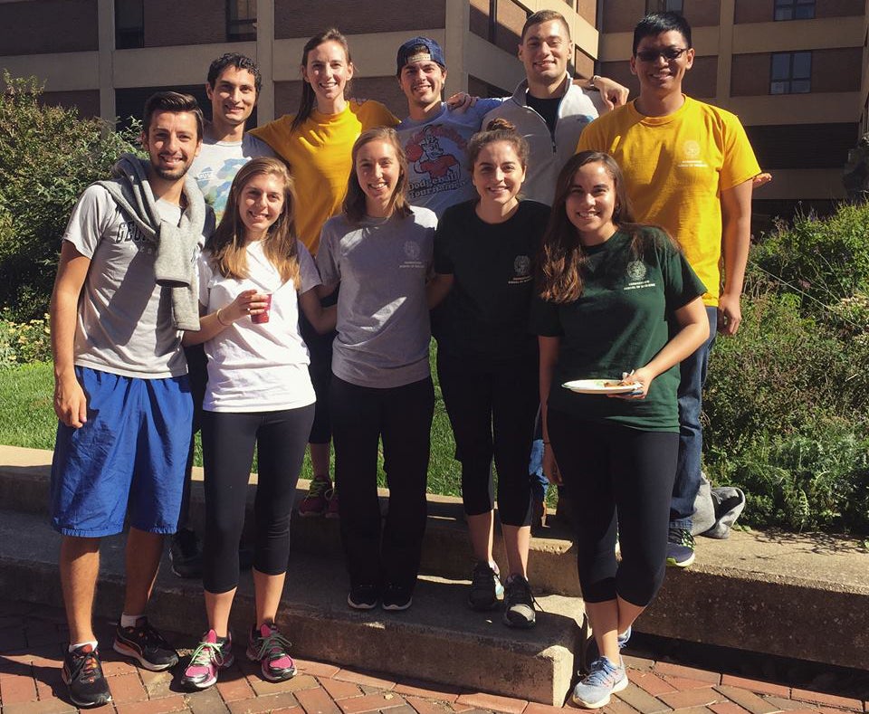 A group of students stands on a paved area near a lawn outdoors