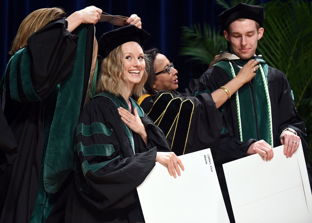 A female medical student smiles as she receives her honorary sash and holds her degree