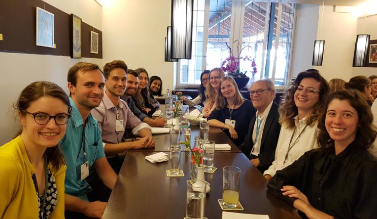 A group of students sits at a long dining table with an older man