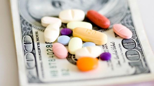 Pills and capsules are piled atop a stack of hundred dollar bills to symbolize the cost of prescription drugs