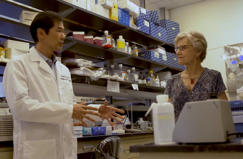 A researcher in white lab coat speaks with a woman