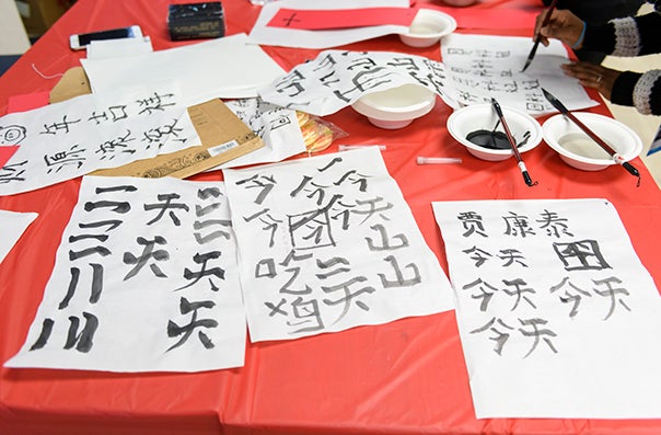 A red tablecloth on which is set white paper with Chinese calligraphy in black ink.