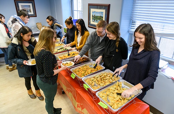 Students file past a table laden with pans of food that other students stand ready to serve them from.