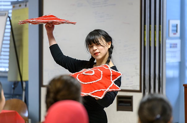 A woman holds two red fans in a graceful position
