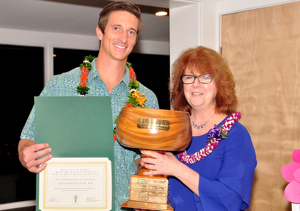 Alex Placek displays a certificate as he stands next to a woman holding a wooden trophy cup