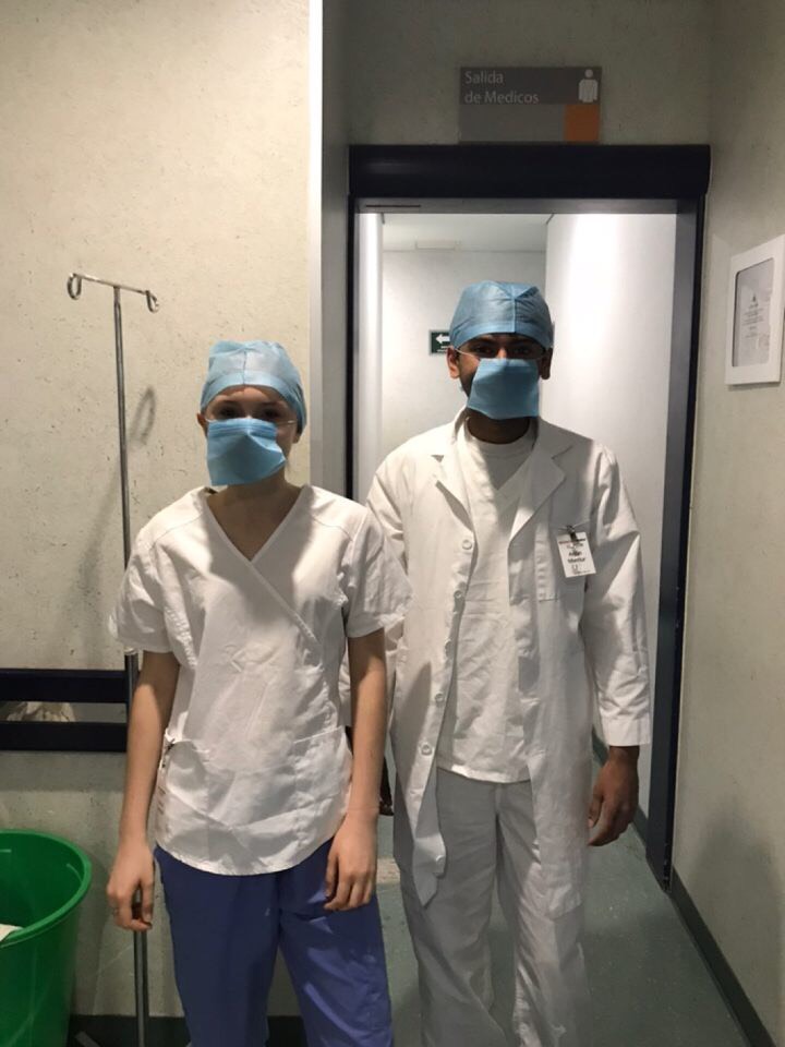 A boy and girl stand next to one another wearing surgical masks, surgical hats, and scrubs.