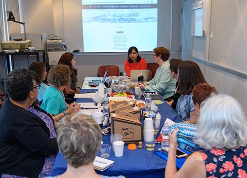 GBCA members sit around a table facing a screen on which an image is projected. The table is filled with notebooks, coffee cups and computers.
