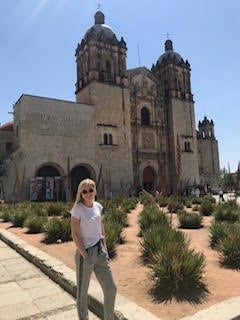 A girl, wearing sunglasses, stands in front of a building.