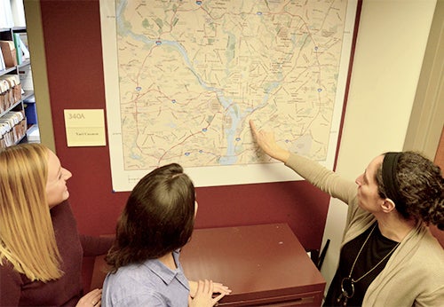 Three women stand and look at a map of the D.C. area; one of the women points at something on the map