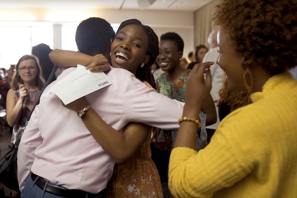 Two individuals hug in joy while another looks on during Match Day festivities