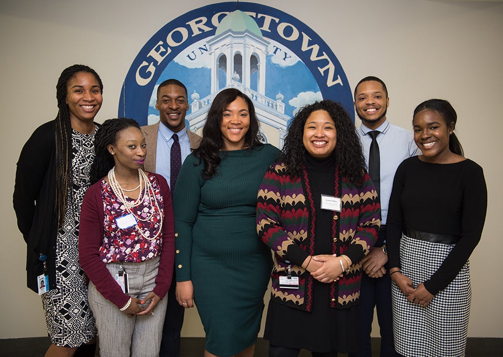 A group of students of color stand together in front of a wall with a mural that says Georgetown