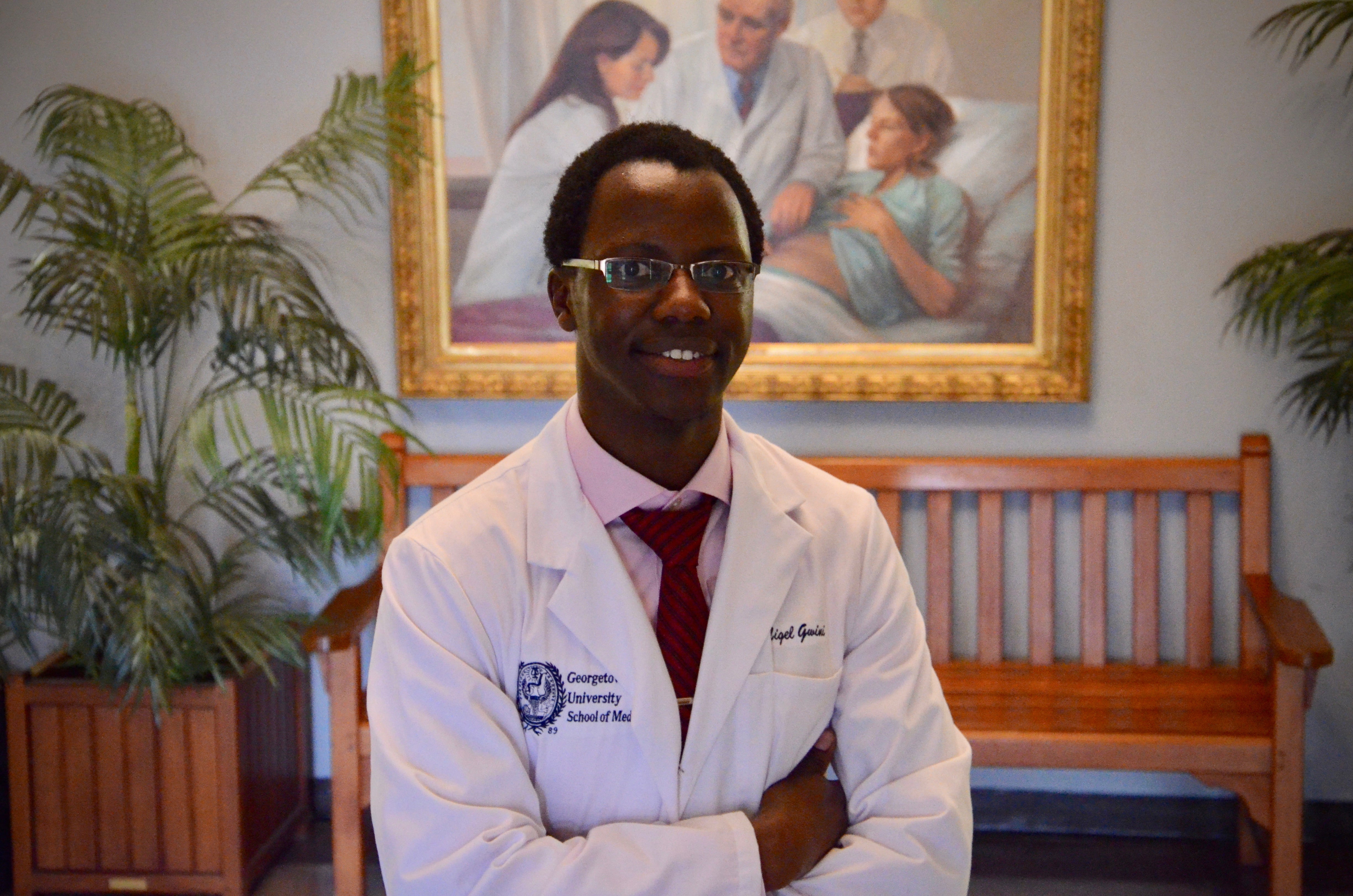 A male medical student stands posing wearing a white coat.