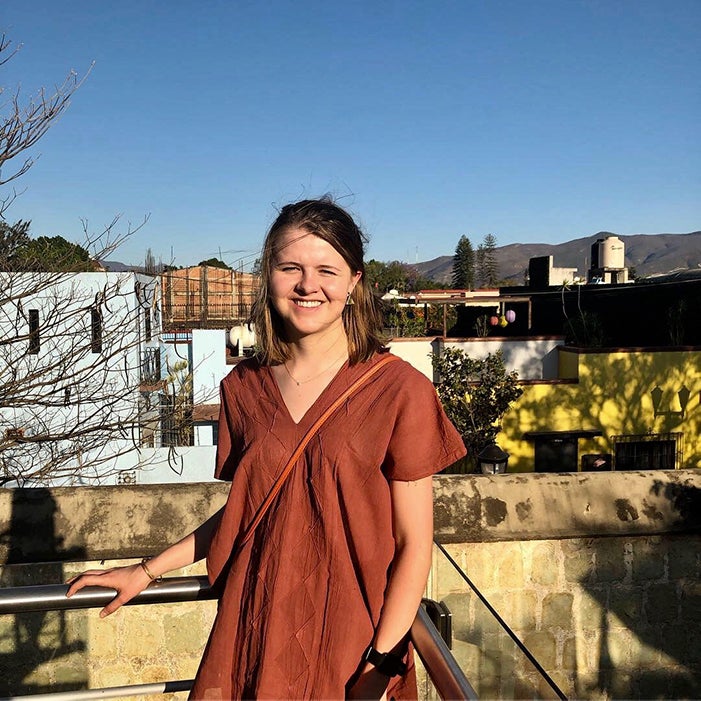 A girl, standing outside, smiles at the camera.