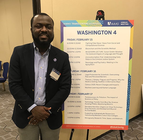 A man stands next to a poster display of the conference schedule