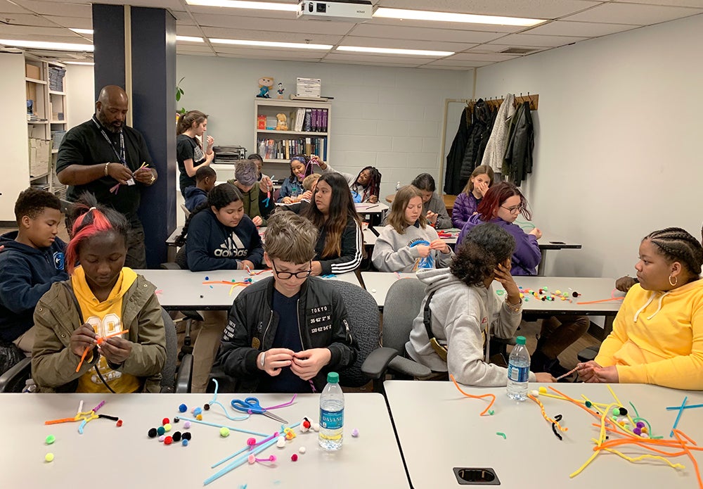 Students sit at tables working with pom-pom balls and chenille stems