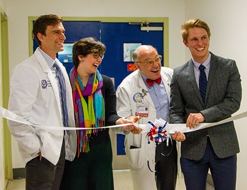 Four individuals stand behind a ceremonial ribbon strung across a hallway