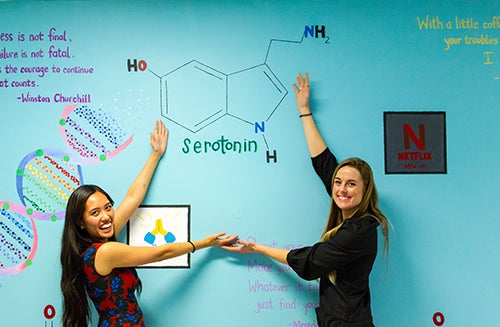 Two individuals stand with arms outstretched to highlight a painted image of a molecule of serotonin.