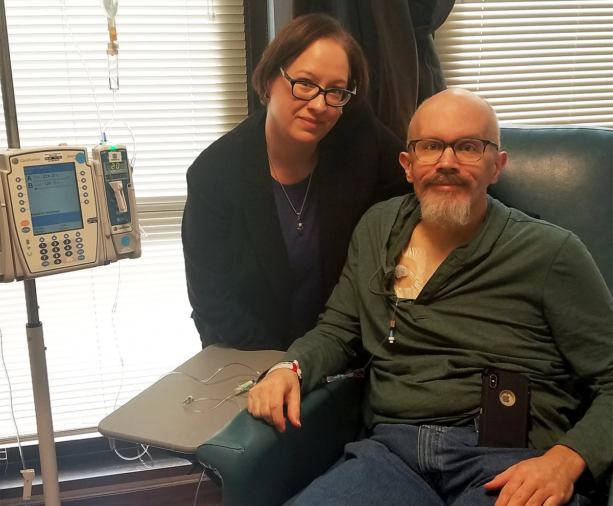 A woman sits next to a man in a chair who is receiving chemotherapy