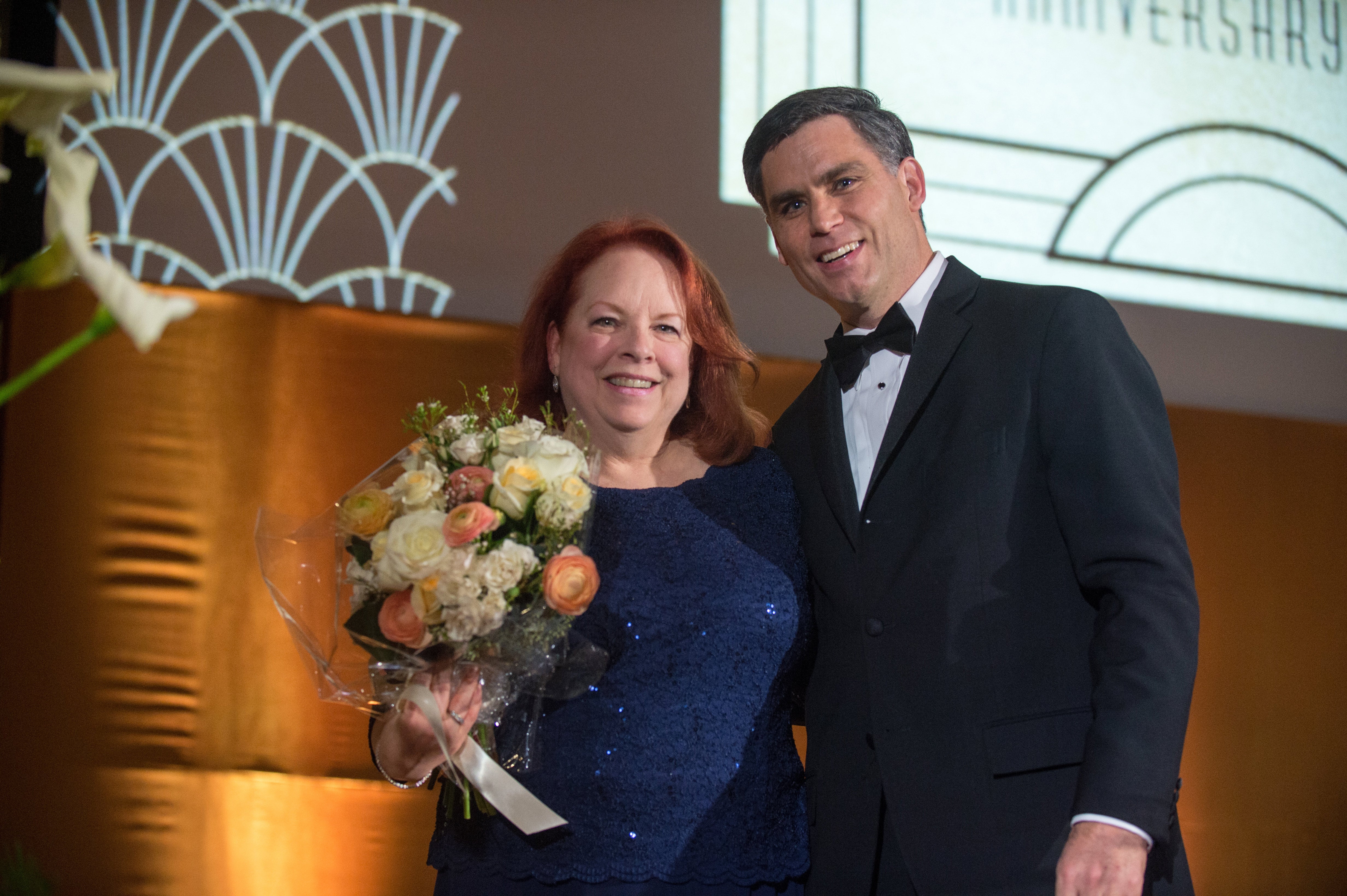 A man and woman stand next to one another holding flowers.