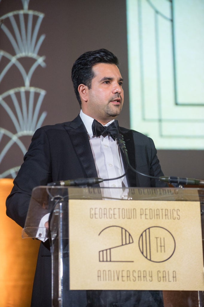 A man stands at a podium dressed in a tuxedo. 