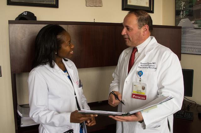 Two doctors talk while holding a clipboard