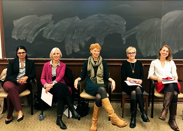 Five women sit in chairs in front of a blackboard