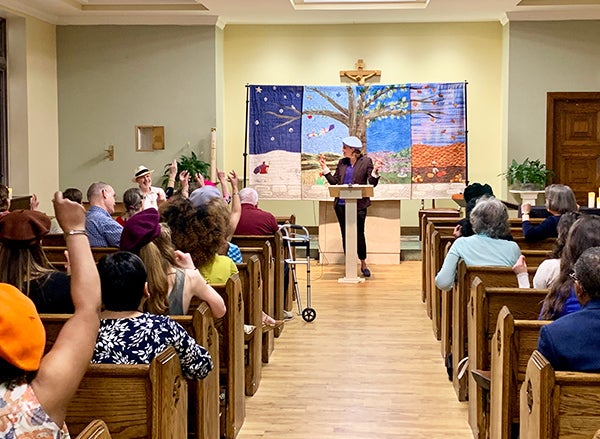 A woman stands at a podium before an audience seated in church pews