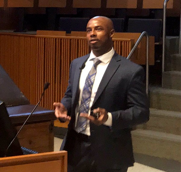 Tyrel Powell speaks from behind a podium in an auditorium