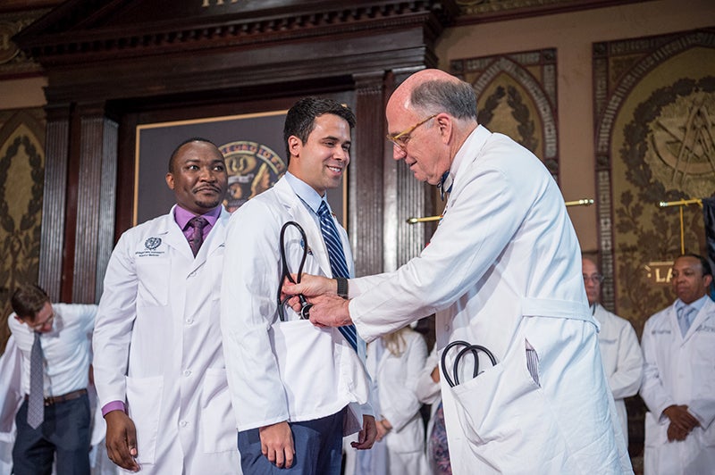 Dean Mitchell puts a stethoscope in the pocket of a medical student