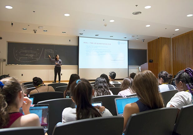 Students sit in an auditorium while an instructor presents a lecture