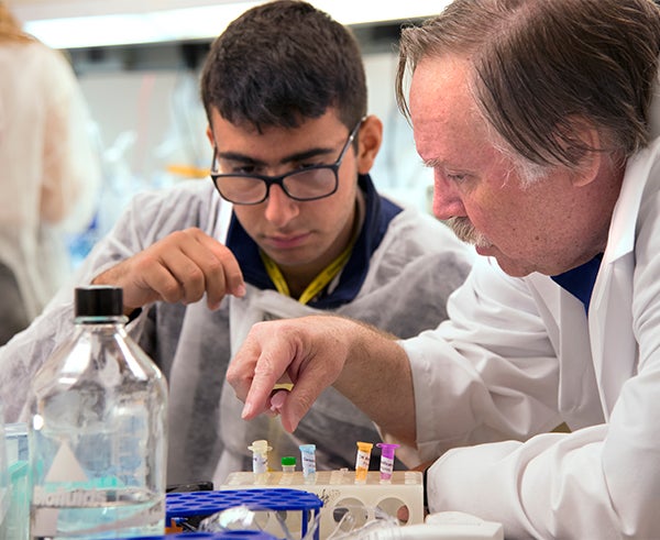 Robert Donahue, in white lab coat, talks with a young male student 