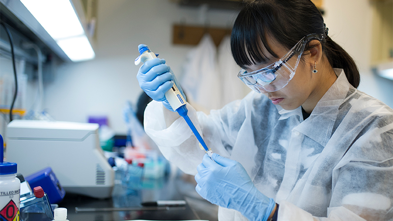 A young woman works at a lab bench with a pipette