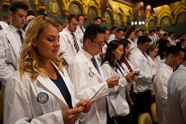 White coated medical students stand and read the Hippocratic Oath.