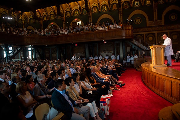 Dean Mitchell stands at a podium addressing a full auditorium 