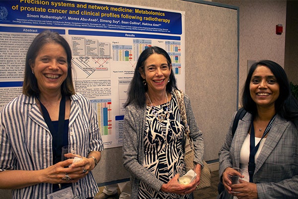 Three conference attendees stand in front of a poster