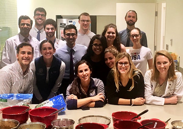 A group of men and women stand together in a kitchen area with food prep materials in front of them