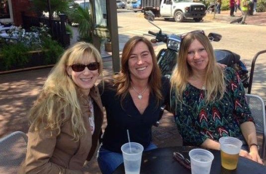 Three women sit together at a table outdoors