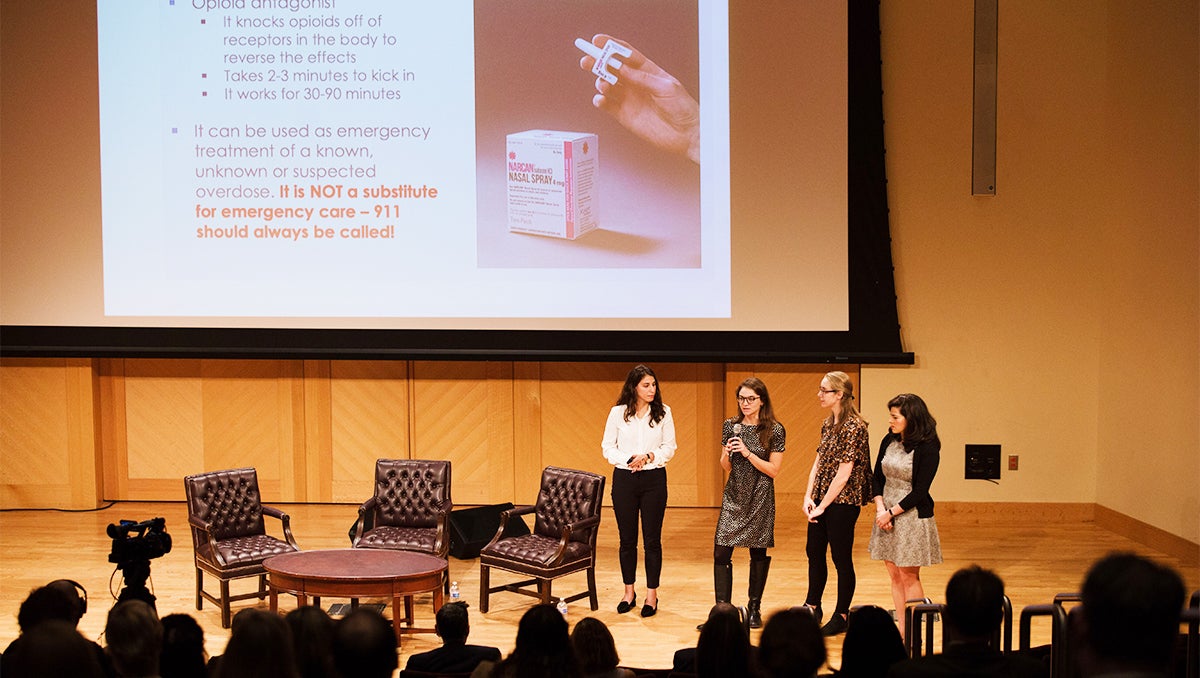 Four women stand on a stage before an audience