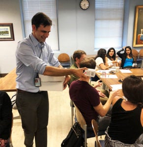 A man hands out a box of medicine to a group of people seated at a table