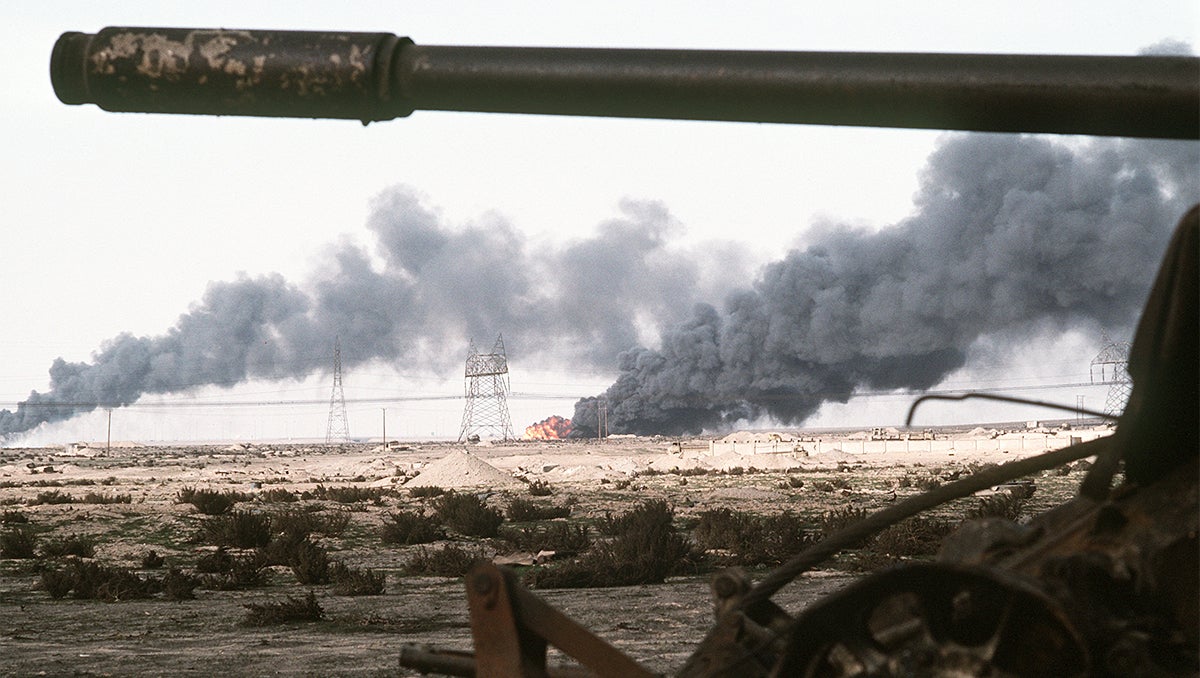 Landscape in Iraq punctuated by fire and smoke, a tank barrel is in the foreground